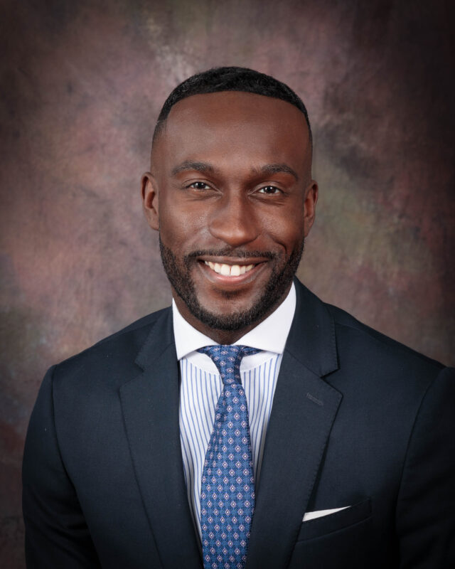 Professional portrait of a smiling man in a suit and tie.